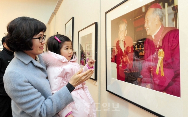 ▲ 김수환 추기경 선종 2주기 기념 특별사진전이 15일 평송 청소년 문화센터 전시실에서 열려 한 시민이 어린 딸에게 사진을 설명해주고 있다./손인중 기자 