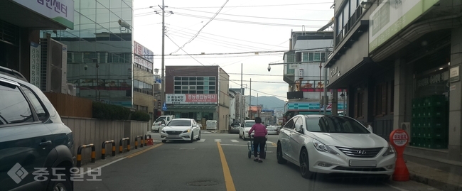 ▲ 지난 21일 오후 홍성 전통시장 주변 2차선 도로에서 여기저기 주차된 차들을 지나 한 할머니가 수레를 밀고 있다. 역시 주차된 차들을 피해 맞은편에서 역주행 하던 차량에 놀란 할머니가 도로를 건너는 데는 한참이 걸렸다. 지난 달 30일 노인 사망사고가 발생한 장소와 멀지 않다.